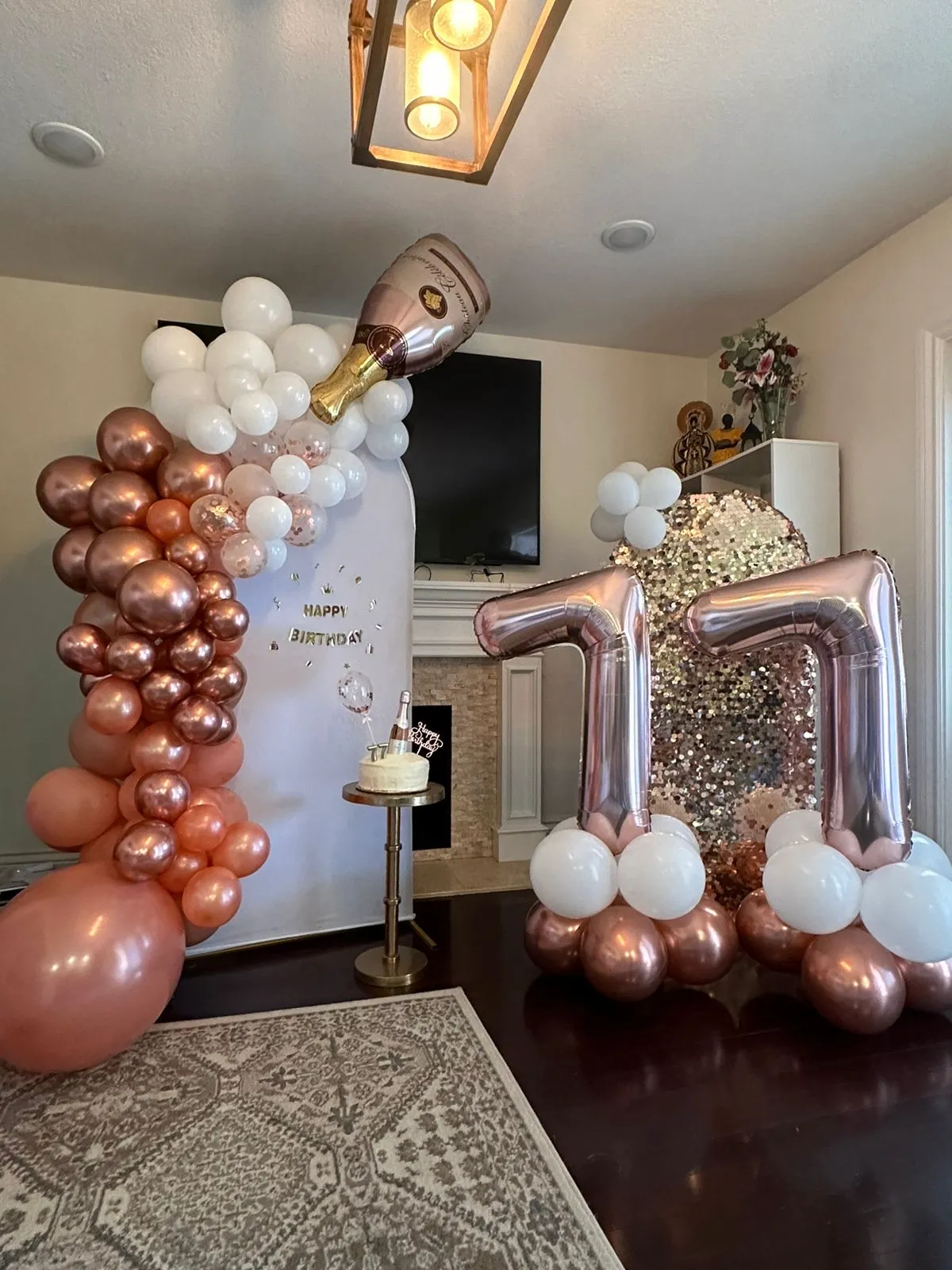 Rose gold and white balloon arrangement with a champagne bottle balloon pouring into a cascade of bubbles, alongside a birthday cake and large number balloons